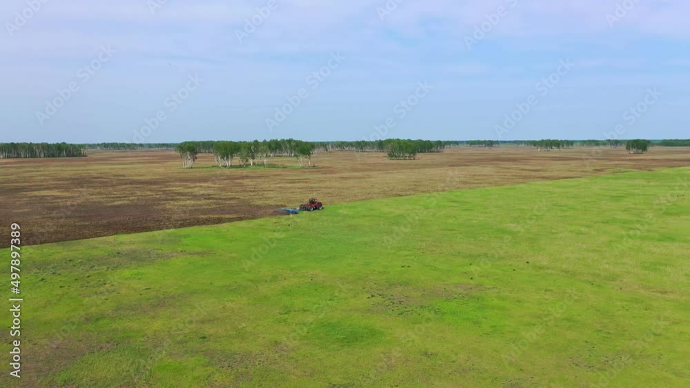 A red tractor with a blue plow cultivates the land. Agricultural equipment. The tractor plows the green meadow. A red tractor with a blue plow cultivates the land. Agricultural equipment. The tractor plows the green meadow.