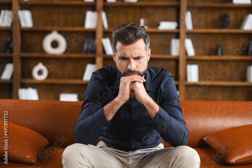 Canvas Print Pensive caucasian guy sitting on the sofa at home or at the office
