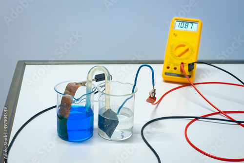 Principle of a rechargeable copper-zinc battery. Blue copper sulphate and transparent zinc sulfate are connected with  a salt bridge. The voltmeter indicates just over 1 volt. Used in chemistry class. photo