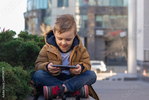 little boy having fun using a smartphone sitting on bench on the background of office building.front view image