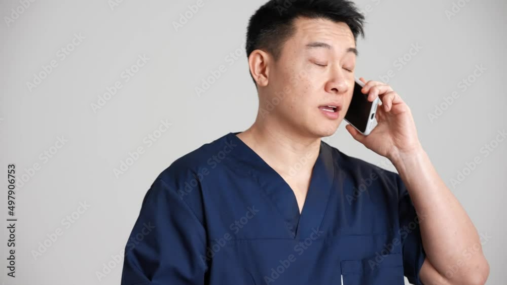 Happy Asian doctor talking with patient by phone in the grey studio