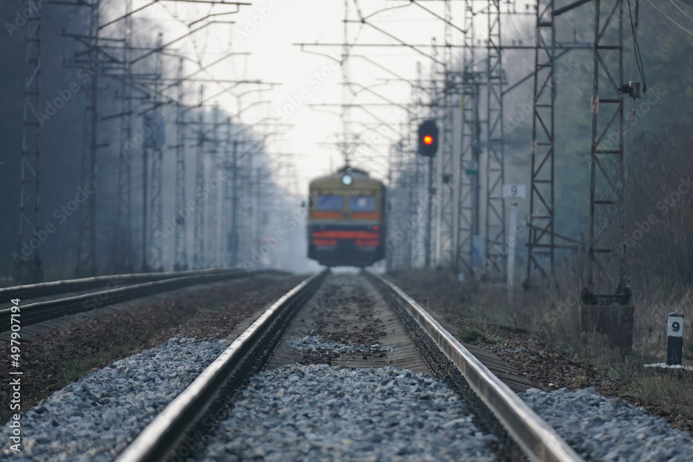 Fototapeta premium Train rides on rails, red traffic light, evening foggy time
