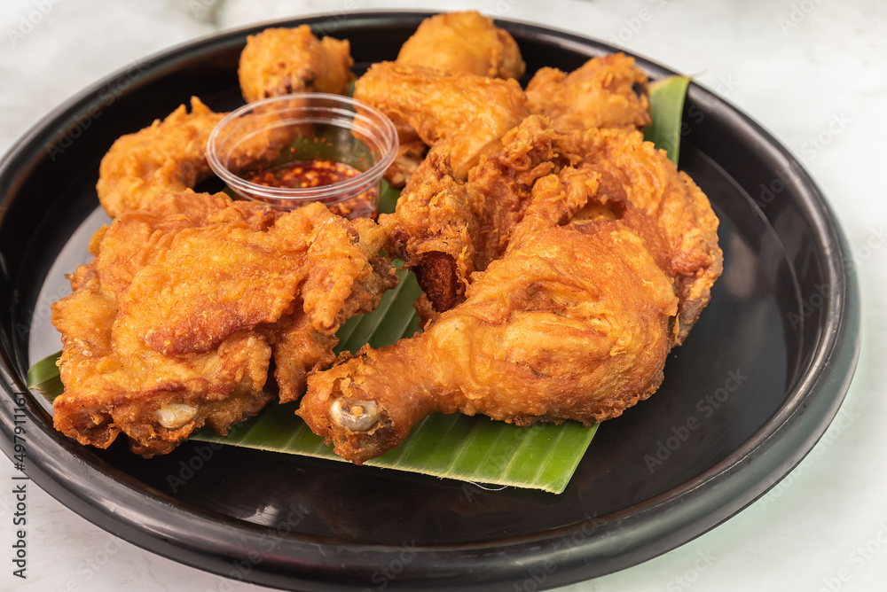 Appetizing fried chicken that sits on a banana leaf in a black plate.