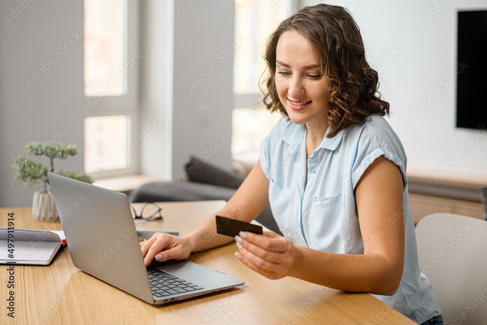Smiling caucasian teenage girl sitting at the laptop, entering credit card number to make an online transaction. Woman ordering food, doing online shopping from home Smiling caucasian teenage girl sitting at the laptop, entering credit card number to make an online transaction. Woman ordering food, doing online shopping from home