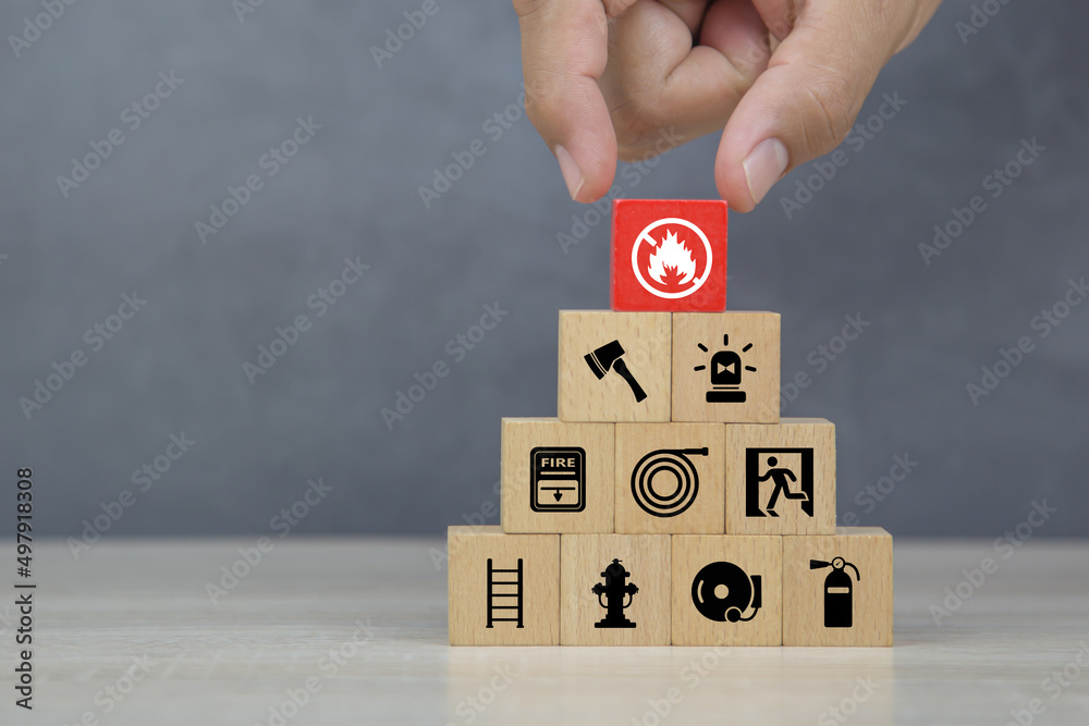 Hand choose wooden block stack with fire prevent icon and door exit sing or fire escape with fire extinguisher and emergency protection symbol for safety and rescue in the building. Hand choose wooden block stack with fire prevent icon and door exit sing or fire escape with fire extinguisher and emergency protection symbol for safety and rescue in the building.