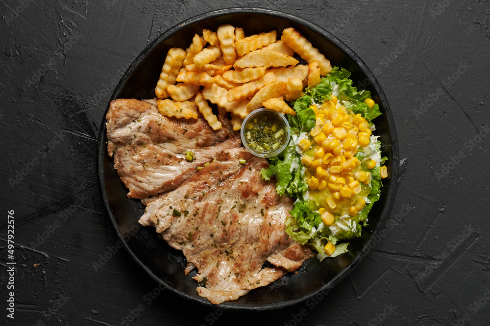 carne de cerdo a la plancha con lechuga y papas fritas sobre un fondo negro carne de cerdo a la plancha con lechuga y papas fritas sobre un fondo negro
