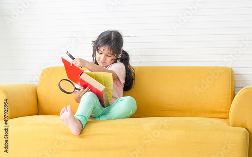 Little kid girl reading book with magnifier on sofa, Happy children playing with magnifying glass in the living room