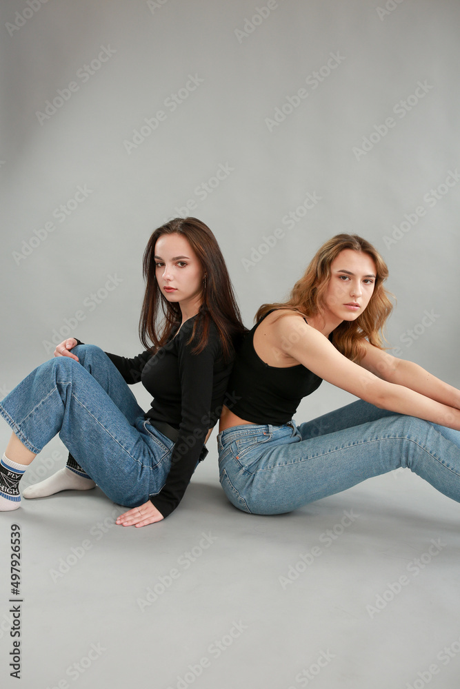 stylish photo shoot of two models blonde and brunette on a gray background in jeans and a black T-shirt. two girlfriends hugging. posing during a photo shoot. young beautiful girls lookbook model stylish photo shoot of two models blonde and brunette on a gray background in jeans and a black T-shirt. two girlfriends hugging. posing during a photo shoot. young beautiful girls lookbook model