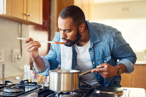 I keep surprising myself in the kitchen. Shot of a man using a wooden spoon to taste his food while cooking.