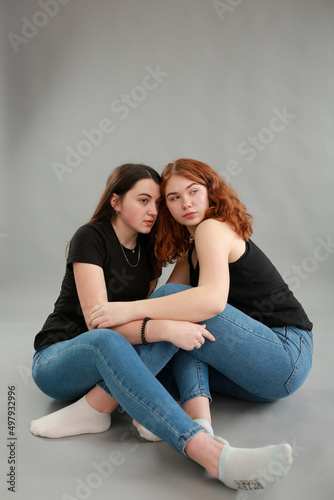 two beautiful girls on a gray background. girlfriends hugging. red hair color. studio photo shoot. female friendship. stop the war © Anhelina Tyshkovets