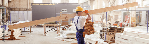 Vászonkép Male builder carrying wooden plank at construction site