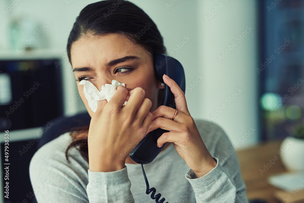 Time to call up the doctor. Shot of a young businesswoman blowing her nose while speaking on a phone in an office. Time to call up the doctor. Shot of a young businesswoman blowing her nose while speaking on a phone in an office.