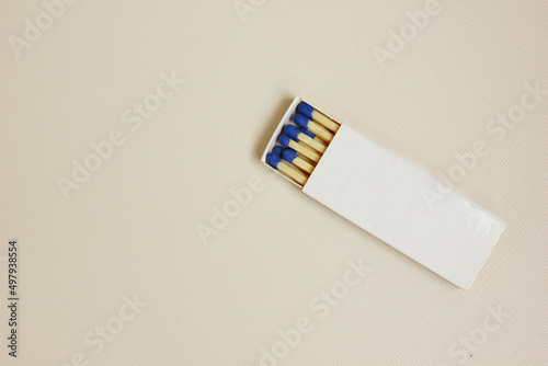 A white matchbox and blue matchsticks on a white background. The box is open. Cooking, hiking, cigarettes. Fire hazardous. Open fire. Copy space for text. top view. flat lay