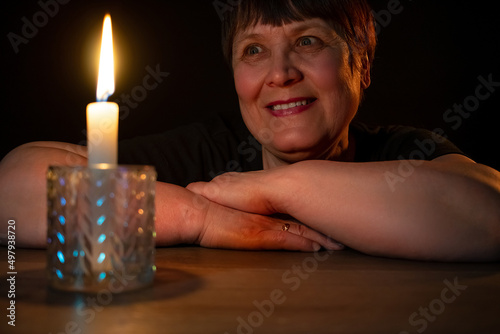 An elderly woman sits in the dark with a burning candle.