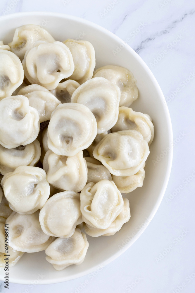Russian meat dumplings on a white plate, top view, close-up. Dumplings with meat filling on a white, marble background. Russian meat dumplings on a white plate, top view, close-up. Dumplings with meat filling on a white, marble background.
