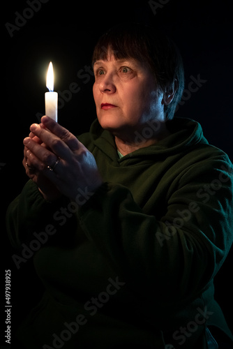 An elderly woman in the dark holds a candle in her hands.