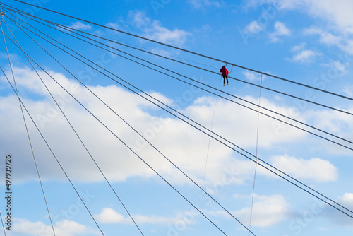 Industrial climber working at height on a suspension bridge against blue sky background © Вера Тихонова