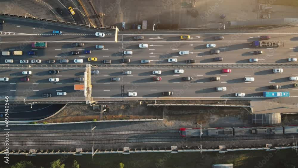 Top view to a busy Moscow highway with heavy traffic on a sunny summer evening. Camera moving above the road showing colorful cars, trucks and a train passing along the railroad.