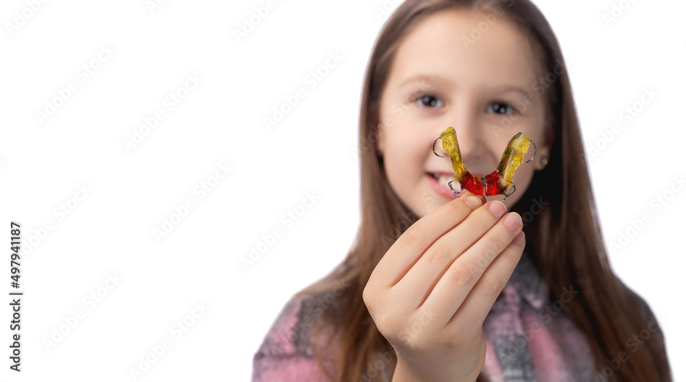 Cute little girl posing in the studio holding an orthodontic appliance in her hand. The concept of oral hygiene in childhood. Photo on a white background. Cute little girl posing in the studio holding an orthodontic appliance in her hand. The concept of oral hygiene in childhood. Photo on a white background.