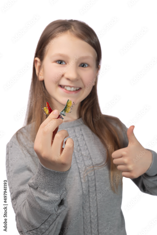 Cute little girl with orthodontic appliance showing thumbs up. The concept of oral hygiene in childhood. Studio photo on a white background. Cute little girl with orthodontic appliance showing thumbs up. The concept of oral hygiene in childhood. Studio photo on a white background.