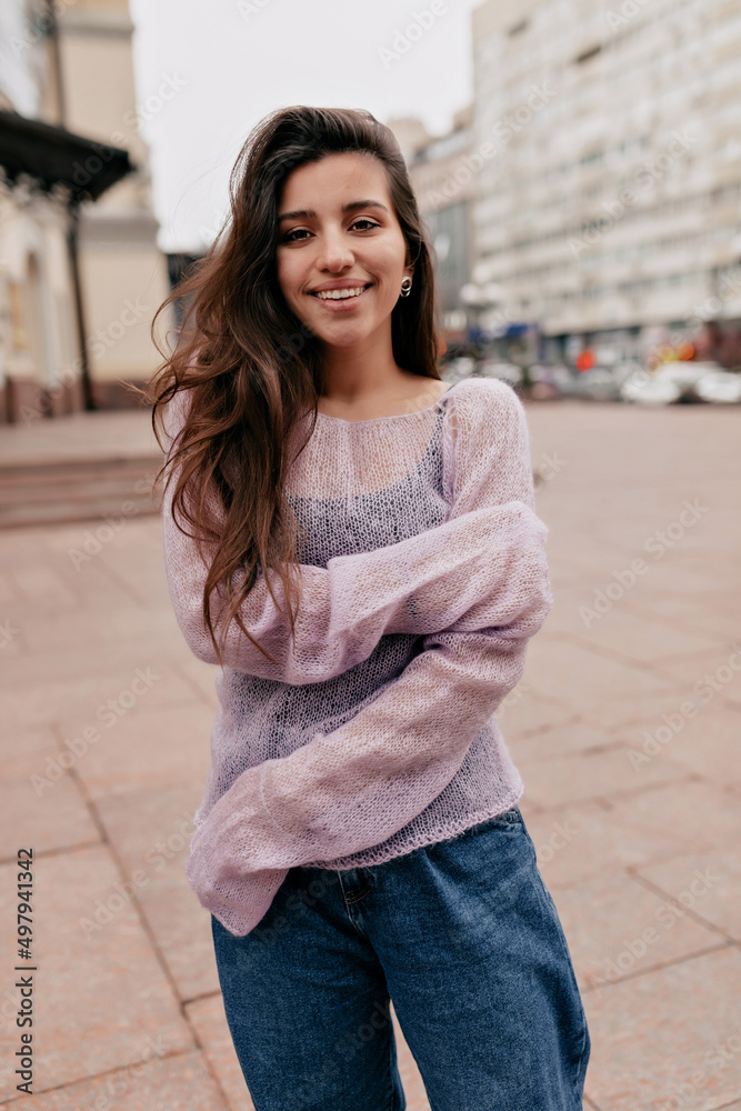 Obraz premium Romantic lovely woman with long wavy dark hair is wearing tender spring thin sweater is posing at camera and smiling 