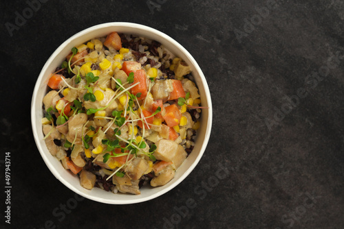 Healthy bowl with wild rice, chicken and vegetables on dark background. Food delivery service and daily ration concept.