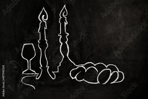 Jewish Shabbat symbols, wine cup for kiddush, two candlesticks with burning candles and challah. drawing on chalkboard