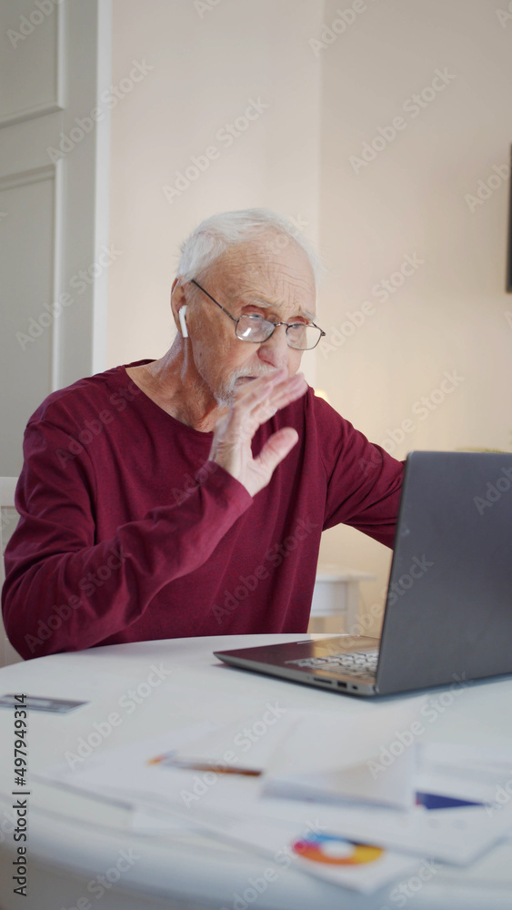 An elderly man starts a call via the Internet. He greets the interlocutor by waving his hand An elderly man starts a call via the Internet. He greets the interlocutor by waving his hand