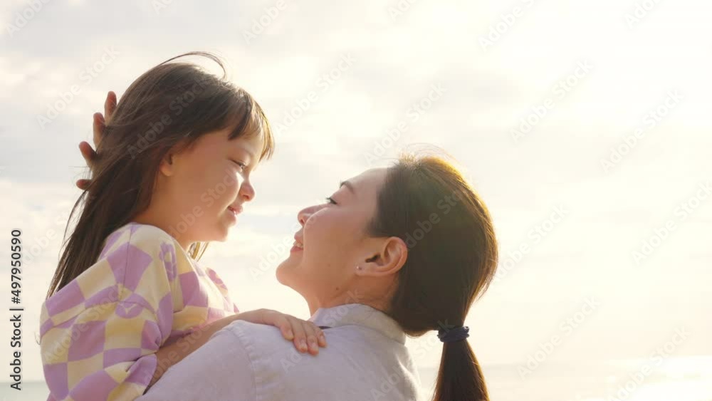 Happy Asian family on beach vacation. Mother carrying and kissing little daughter while walking on tropical beach at summer sunset. Mom and child girl kid enjoy and fun outdoor lifestyle on the beach Happy Asian family on beach vacation. Mother carrying and kissing little daughter while walking on tropical beach at summer sunset. Mom and child girl kid enjoy and fun outdoor lifestyle on the beach