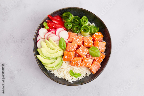 Poke bowl with salmon tuna, rice, avocado, cucumber, radish, pepper, sesame seeds on grey background. Close-up. Hawaiian diet food with fish, pokebowl. Top view.  photo