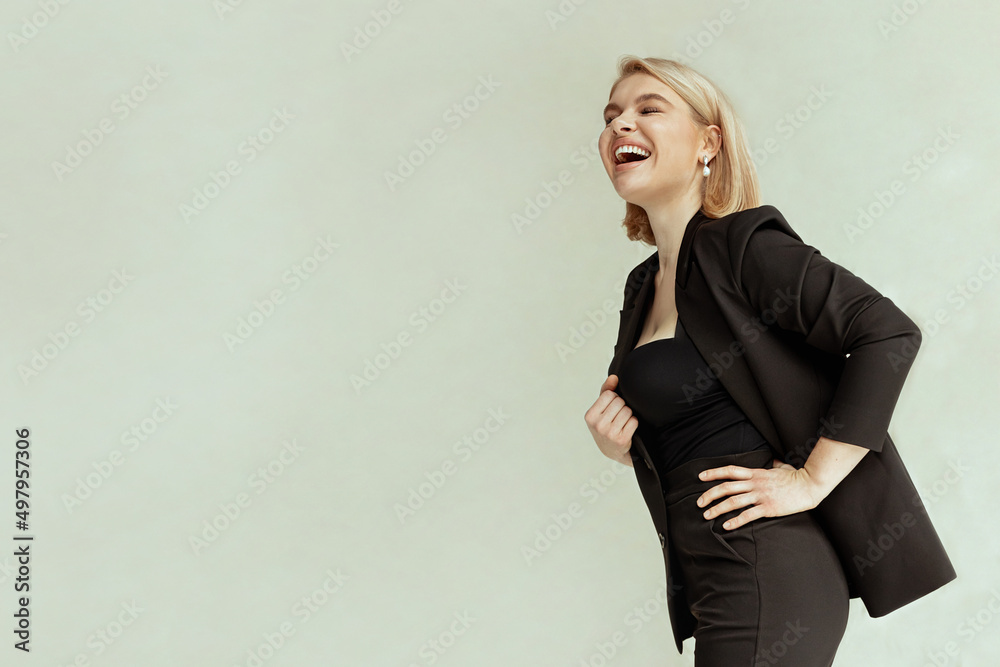 Obraz premium Young blonde woman in business jacket with short haircut celebrating success with emotional admiring smile concept of winner. Stylish girl on a beige background