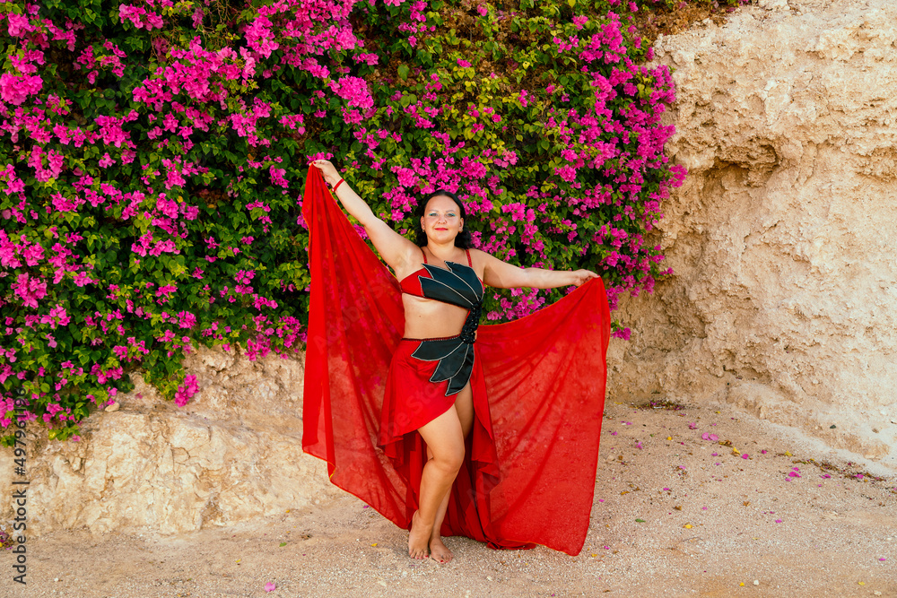 A brunette woman in a red oriental dance costume dances on the street.