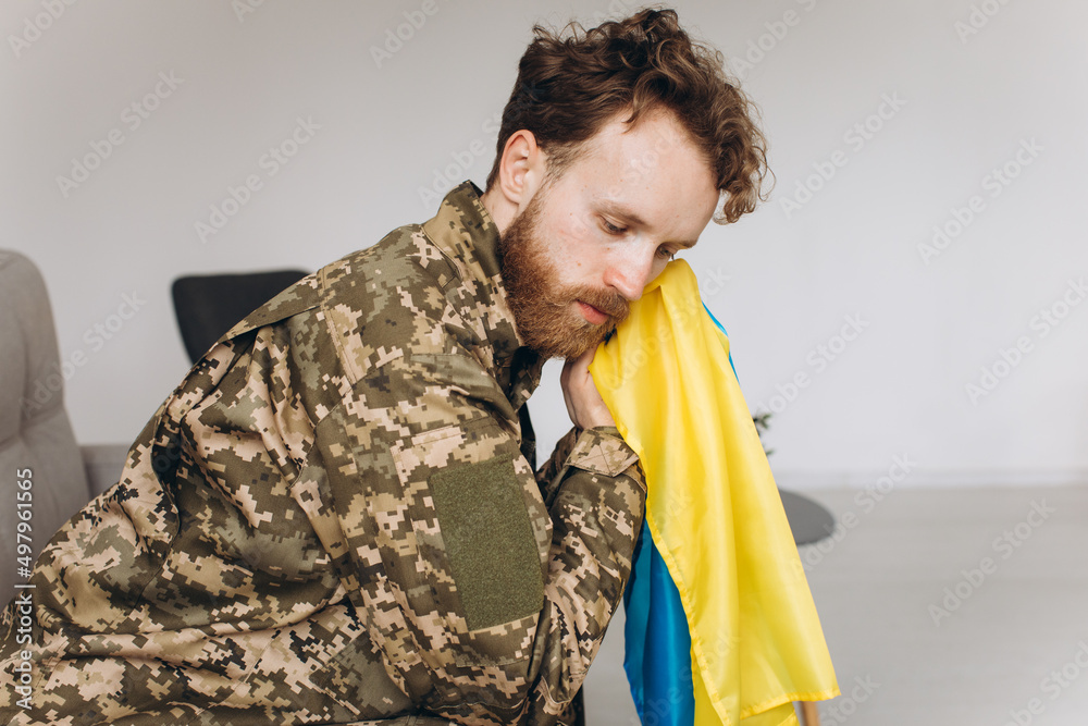 Portrait of an emotional young Ukrainian patriot soldier in military uniform sitting on the office on the couch holding a yellow and blue flag. Portrait of an emotional young Ukrainian patriot soldier in military uniform sitting on the office on the couch holding a yellow and blue flag.