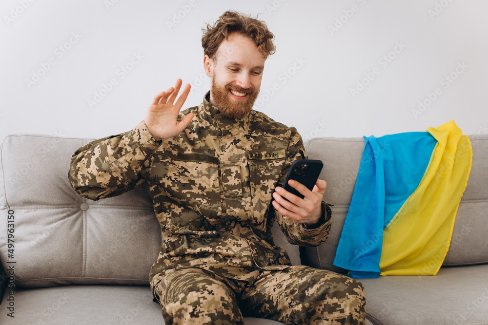 A Ukrainian soldier in military uniform is sitting on a sofa in the office and talking on the phone