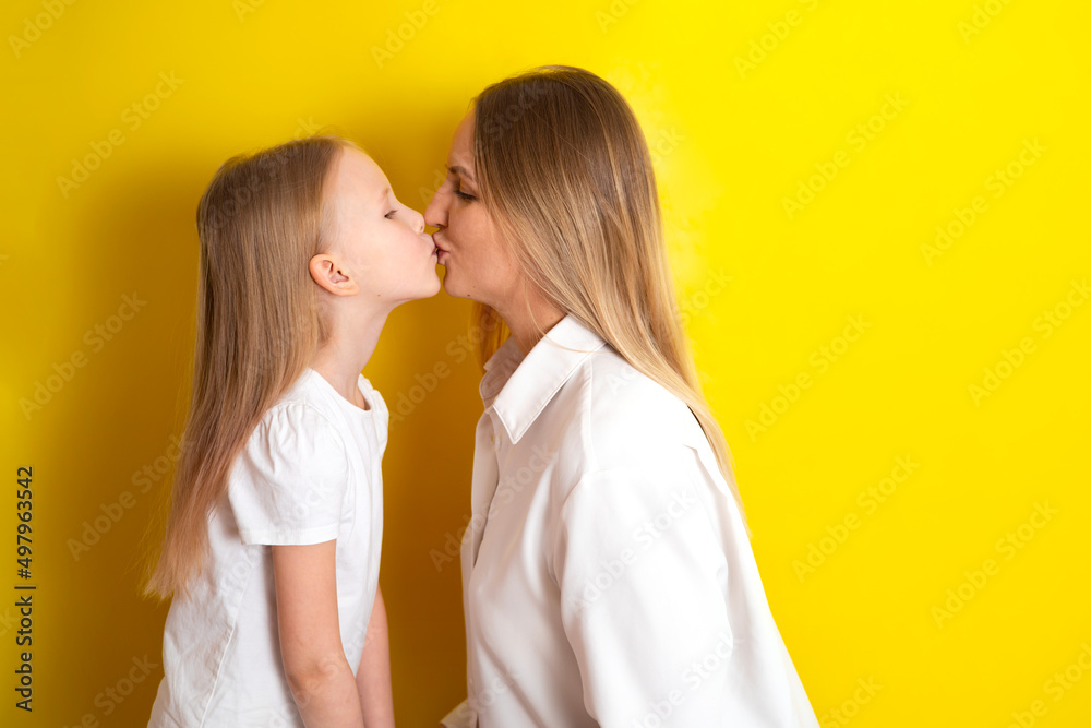 Cute beautiful mother and daughter in white clothes. Embrace the family. Yellow background place for text Cute beautiful mother and daughter in white clothes. Embrace the family. Yellow background place for text
