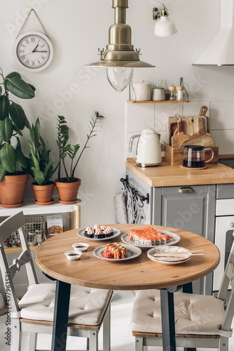Sushi on wooden table in the kitchen. Scandinavian style. White wooden background. Bright kitchen interior. sushi with chopsticks. sushi on a plat. table setting for dinner. modern interior. 