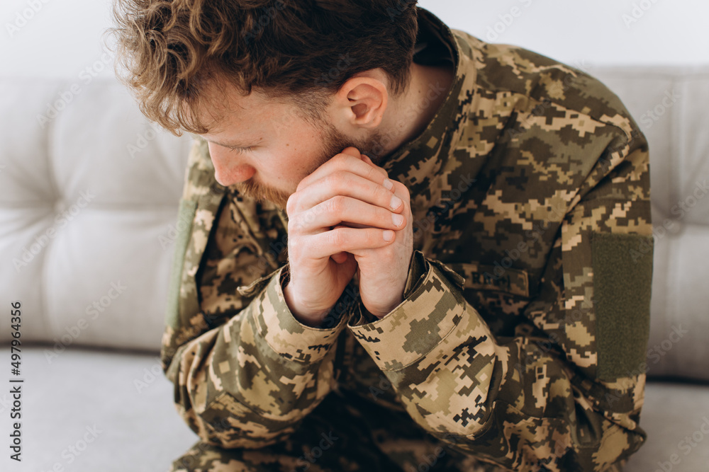 Portrait of emotional young bearded Ukrainian patriot soldier in military uniform sitting on the office sofa