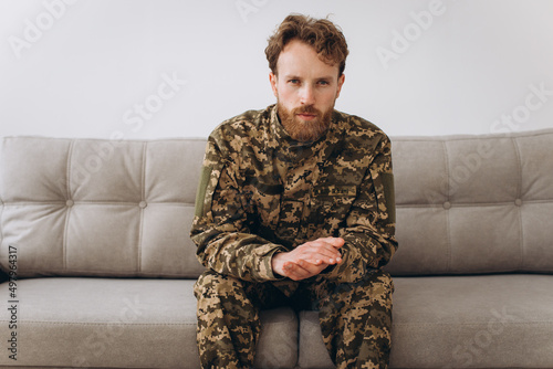 Portrait of emotional young bearded Ukrainian patriot soldier in military uniform sitting on the office sofa © anatoliycherkas