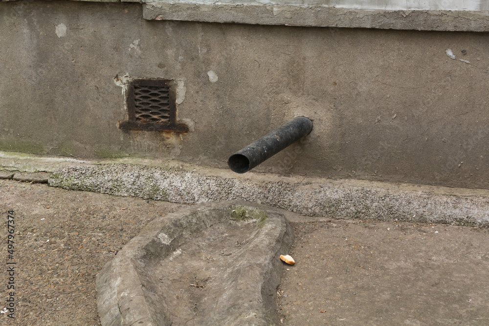 Black plastic rainwater drain pipe at the base of the house. Stock