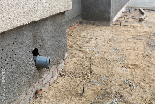 A plastic pipe for draining rainwater installed at the base of the house. Sand, gravel and iron reinforcement at the base of the house, the process of repairing the foundation blind area.