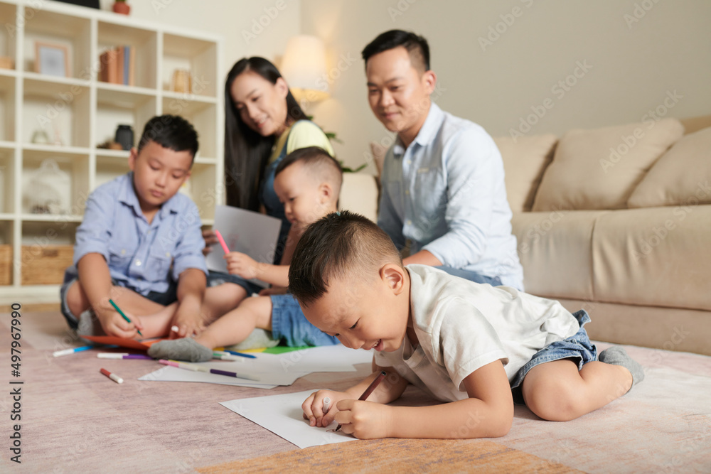 Smiling parents looking at their three sons drawing pictures on floor Smiling parents looking at their three sons drawing pictures on floor