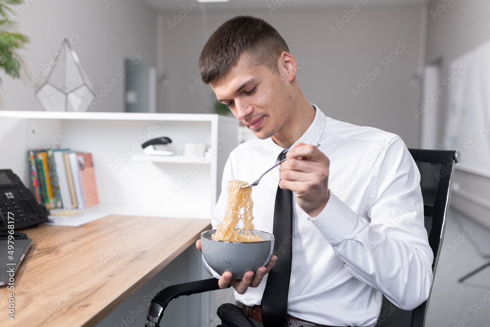attractive young man in the office eating instant noodles attractive young man in the office eating instant noodles