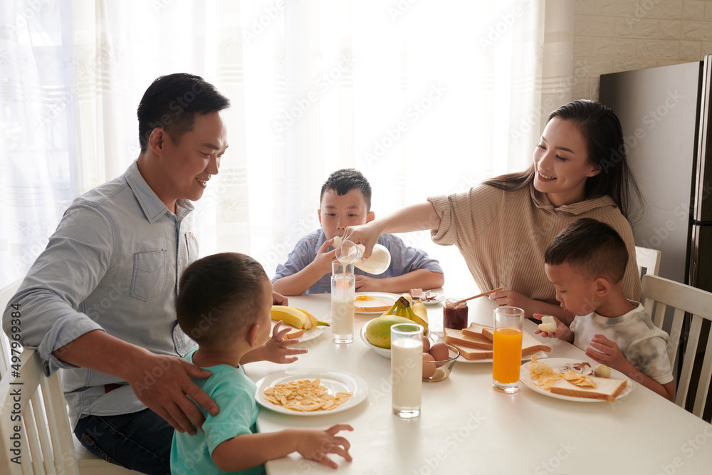 Smiling woman pouring milk for husband and sons at breakfast table Smiling woman pouring milk for husband and sons at breakfast table