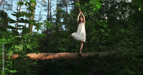 Young woman relaxing outdoors, she do tree position. woman balansed on one leg on a fallen tree. In harmony of nature. photo