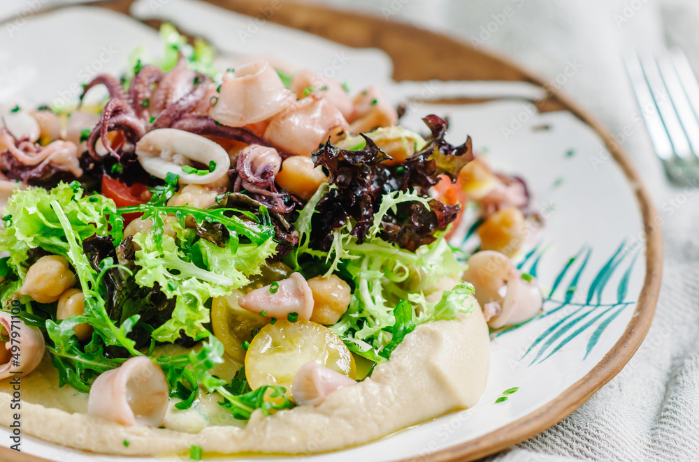 Salad with chickpeas, baby squid, baby octopus, cherry tomatoes, lettuce, arugula and hummus. Italian-French dish from the island of Corsica Salad with chickpeas, baby squid, baby octopus, cherry tomatoes, lettuce, arugula and hummus. Italian-French dish from the island of Corsica