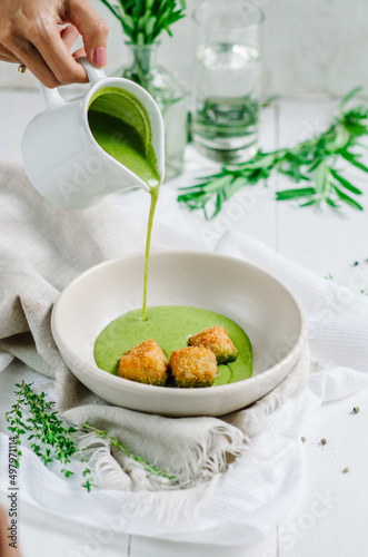 Green vegetable cream soup with fried white fish in a white bowl. Soup is poured into a bowl