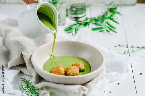 Green vegetable cream soup with fried white fish in a white bowl. Soup is poured into a bowl