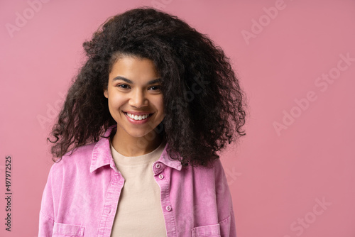 Portrait of beautiful African American woman with toothy smile, curly hairstyle looking at camera isolated on pink background. Dental, health care concept 