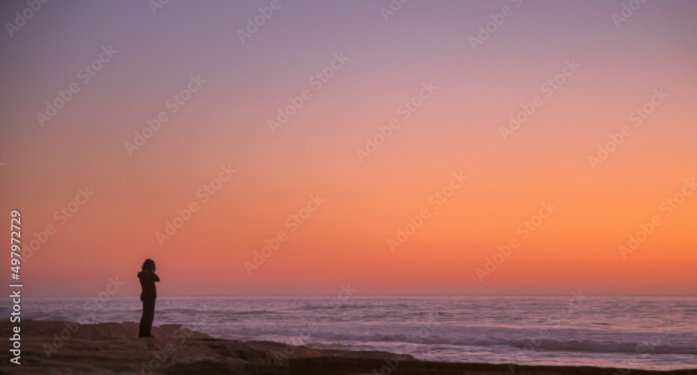 solitary woman in twilight at the seashore contemplates the ocean