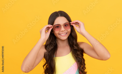 happy teen girl in summer glasses has curly hair on yellow background, summer fashion